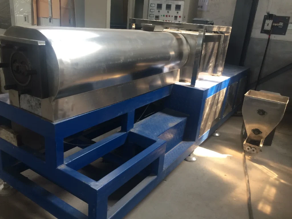 Grande plano de fábrica com uma linha de extrusão de duplo parafuso de 75 mm em frente a secadores de aglomerado inoxidável e torres de arrefecimento duplas numa moderna fábrica de alimentos.