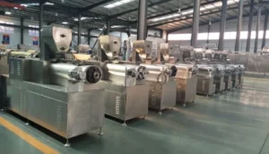 High-resolution hero image of a stainless-steel double screw extruder machine line in a spotless food-processing hall, two operators in hygienic suits inspecting the equipment.
