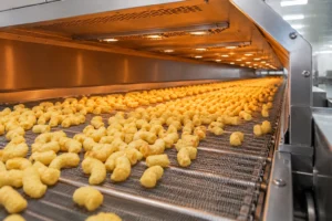 Puffed snacks moving evenly on a stainless steel mesh belt inside a continuous belt dryer for controlled moisture removal and crisp texture.